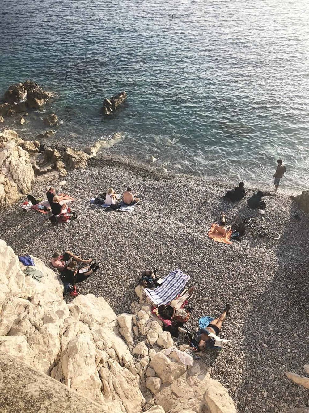Scenic beach with rocks, pebbles, and people relaxing by the water, ideal for seaside vacation and coastal exploration.