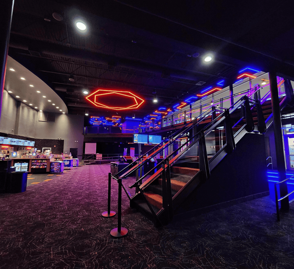 Bright neon-lit staircase in a modern entertainment venue with lounge area and digital screens.