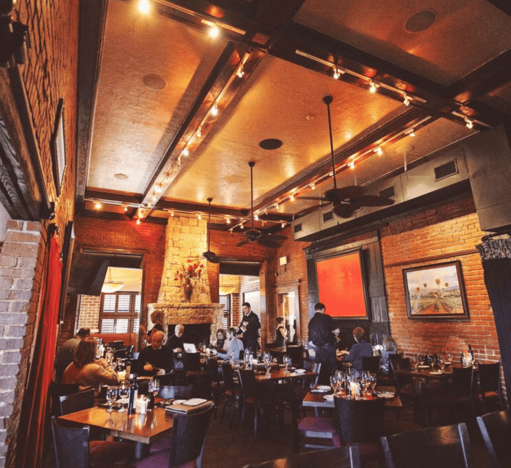 Cozy upscale restaurant interior with brick walls, warm lighting, and fireplace, perfect for fine dining and special occasions.