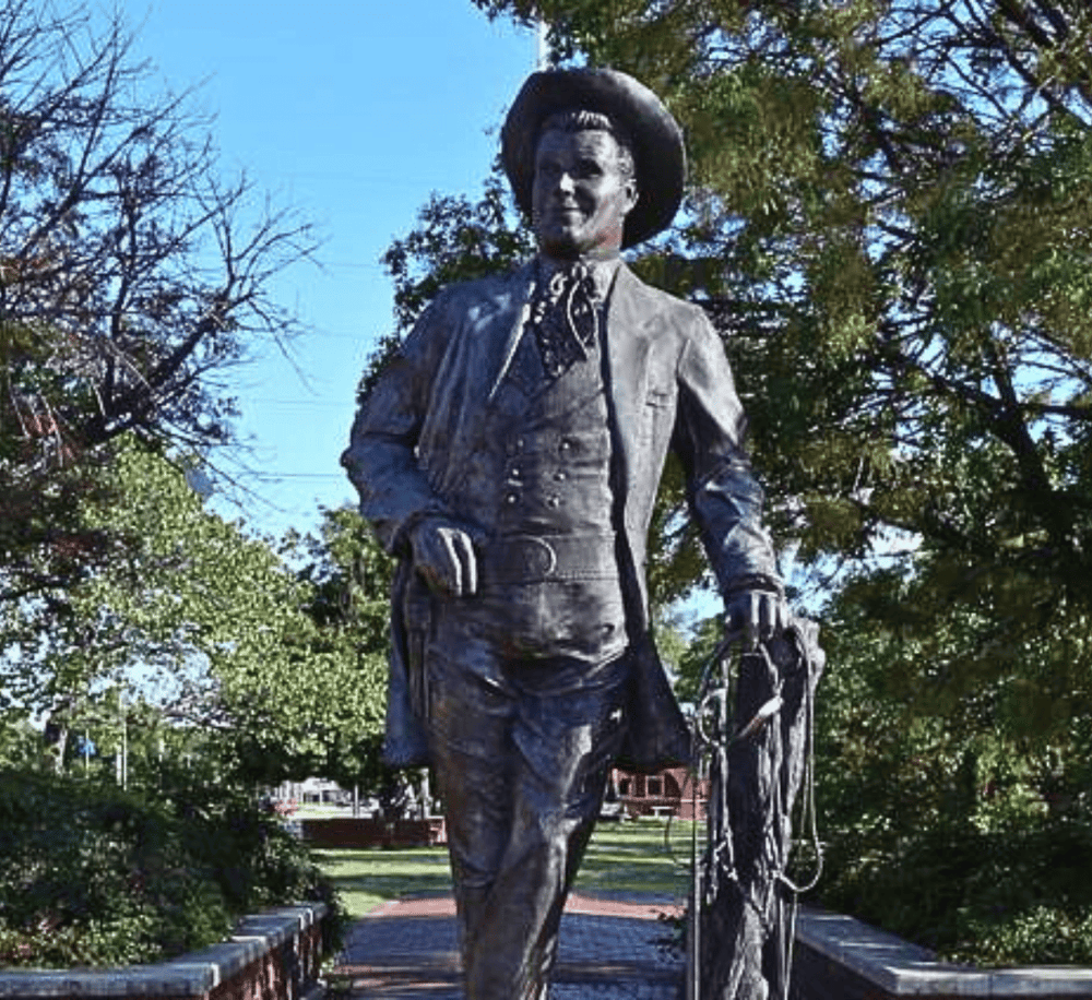 Walking tour guide statue in a park with trees and blue sky in the background.