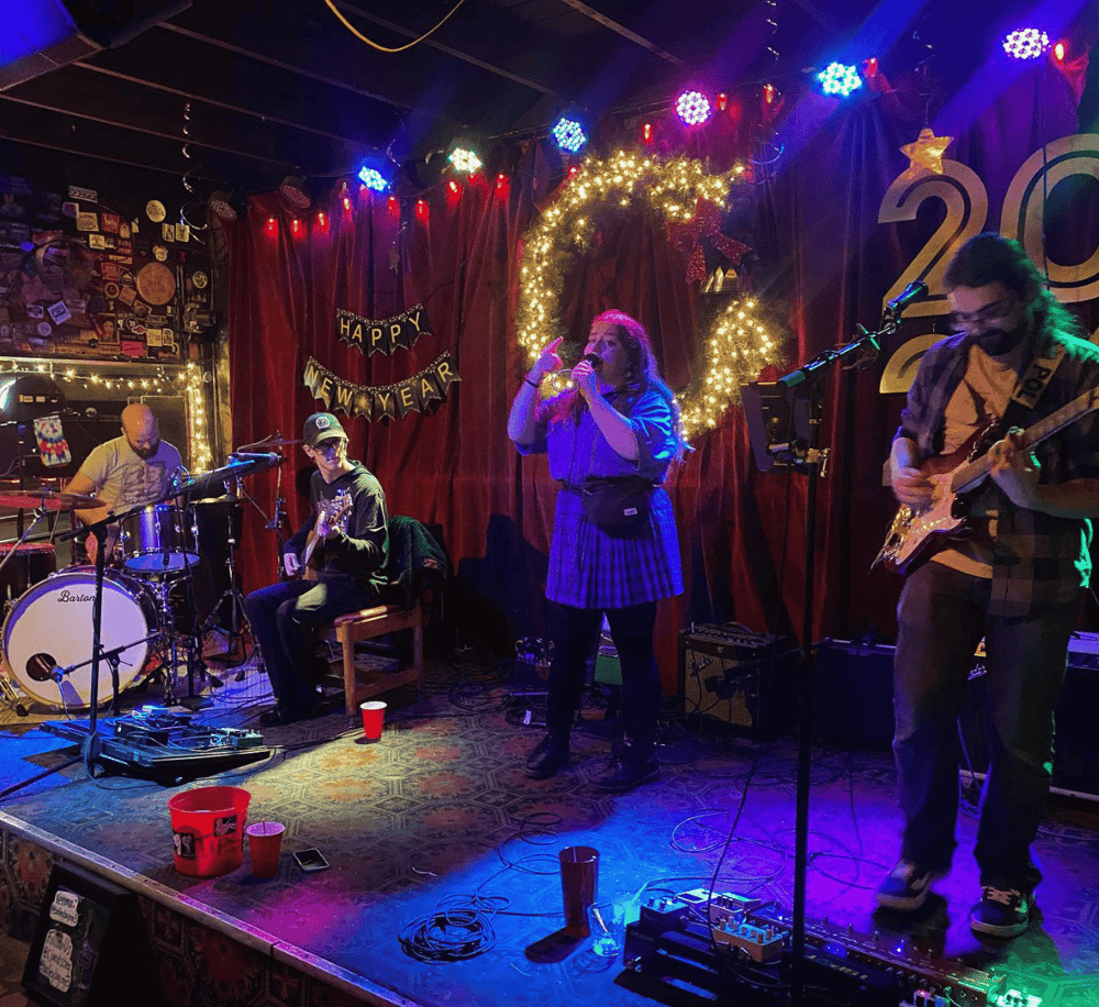 Live band performing at a festive holiday celebration in a decorated venue with "Happy New Year" banner.