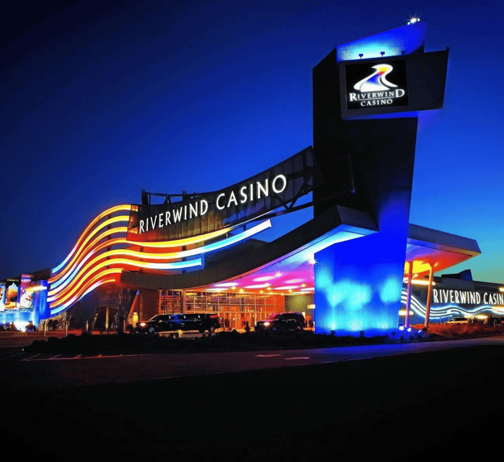 Colorful night view of Riverwind Casino with neon lights and signage illuminated.
