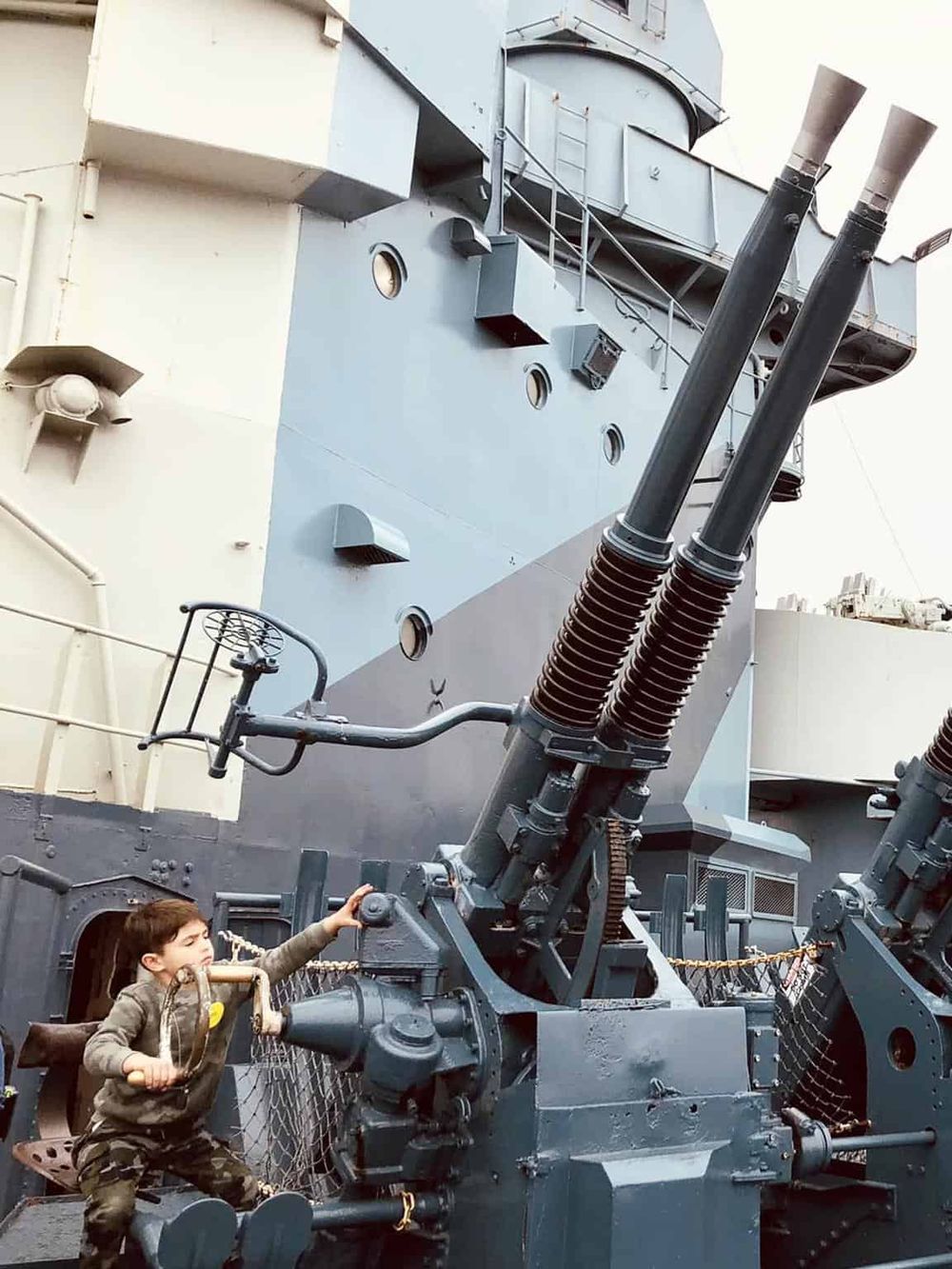 Massive naval gun turret on a battleship with a young boy playing nearby, showcasing maritime military equipment and naval history.