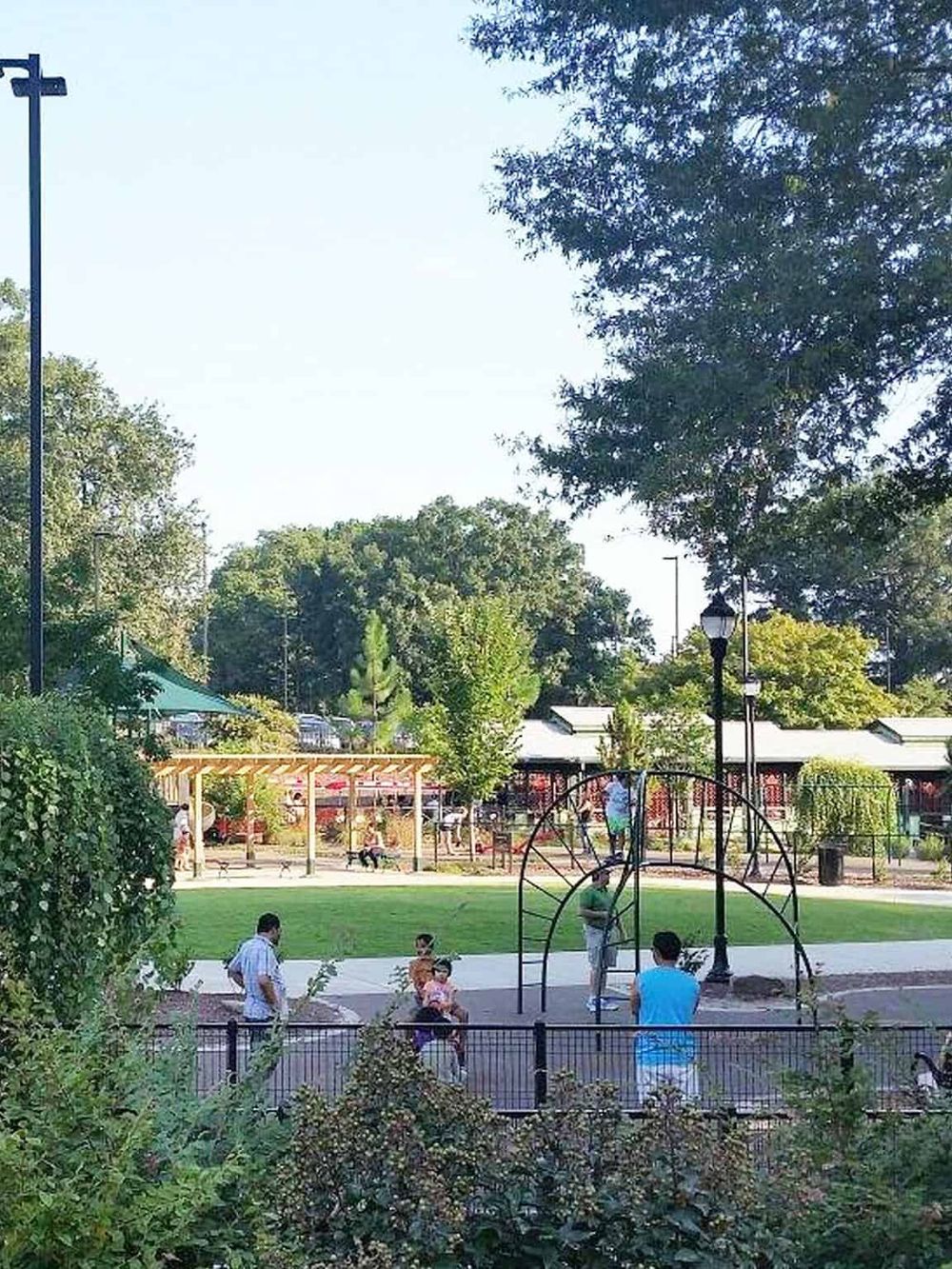 Playground park with kids, adults, and swing set in a lush green outdoor area.