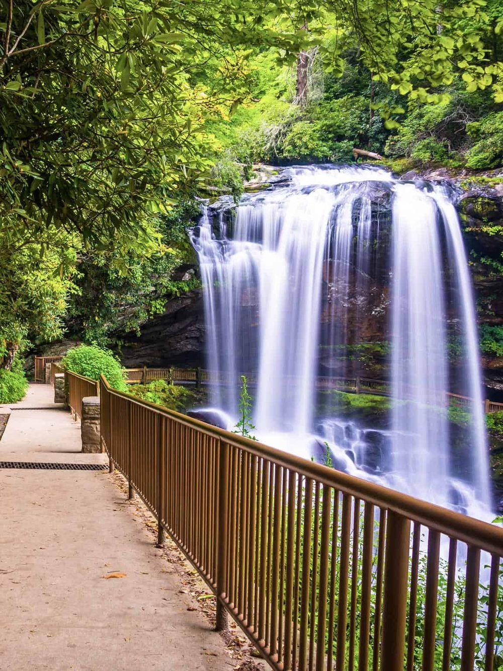 Serene waterfall with lush greenery and a walkway in the scenic natural park setting.