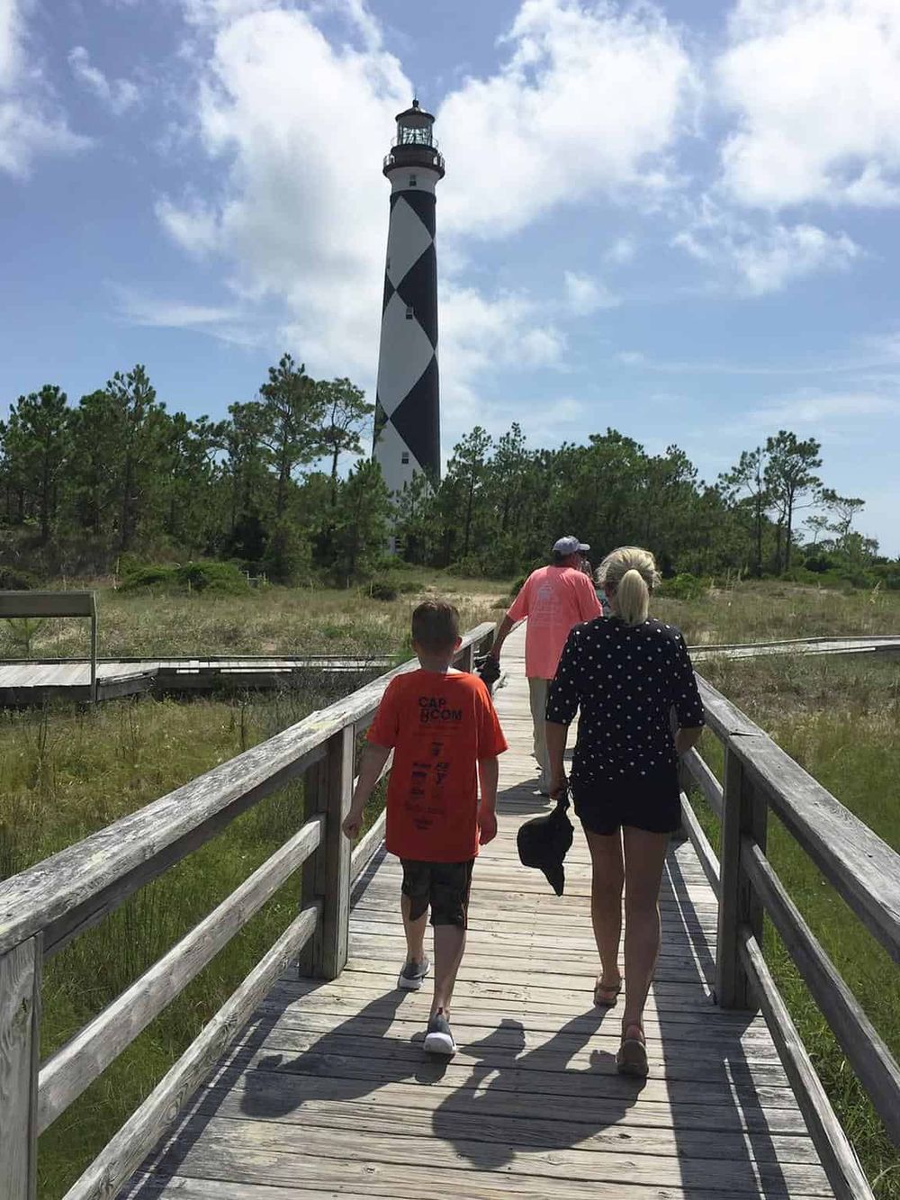 Lighthouse at Cape Hatteras National Seashore with visitors walking on wooden boardwalk.