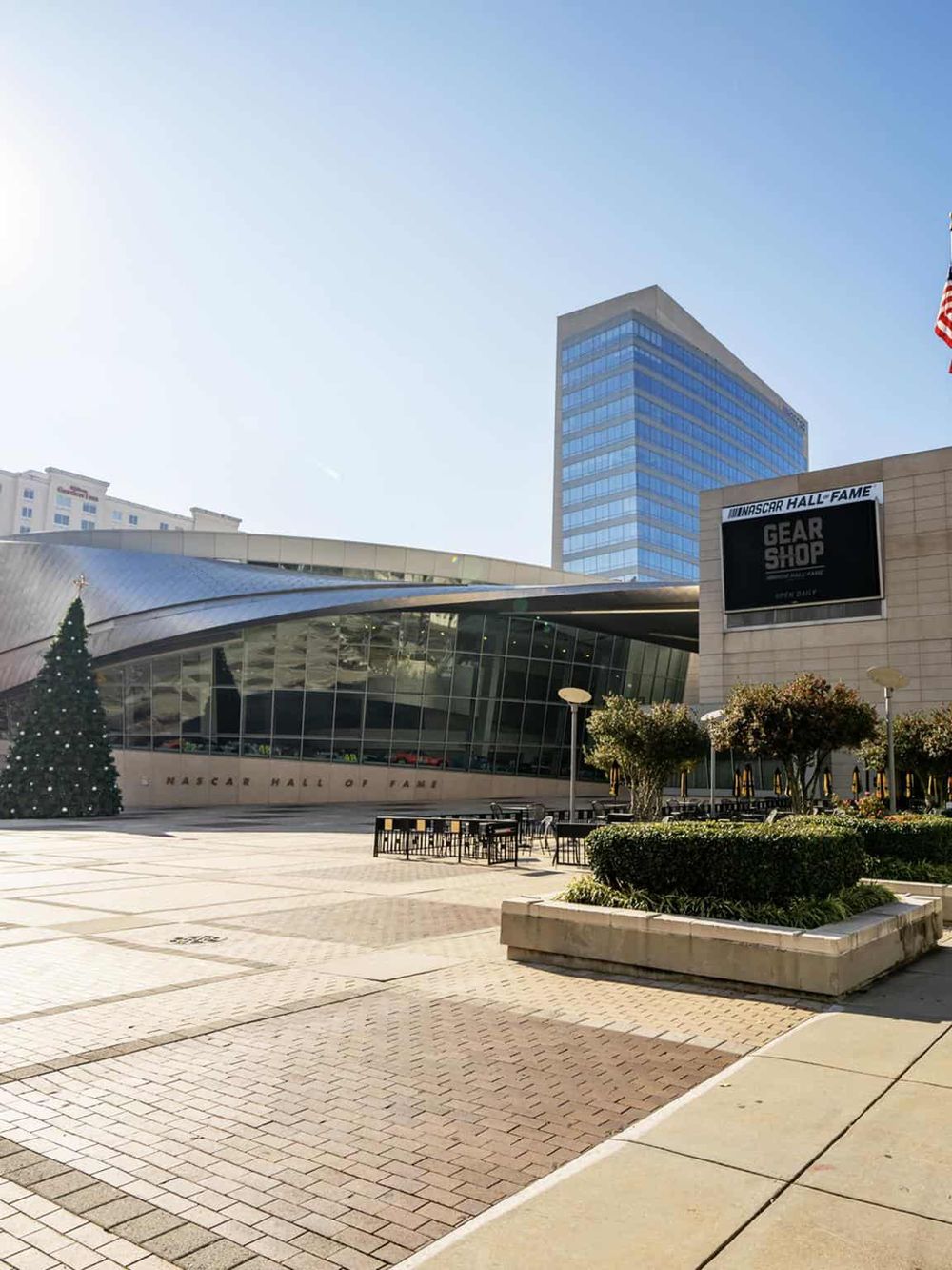 Modern NASCAR Hall of Fame building with glass facade and festive Christmas tree outdoors.