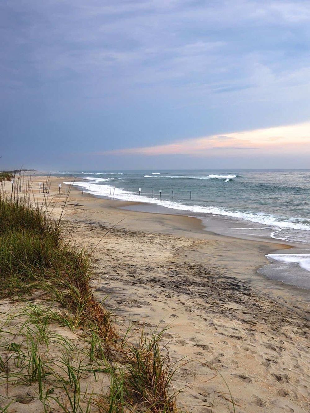 Seaside beach with sand dunes, ocean waves, and cloudy sky, ideal for beach directions and coastal navigation.