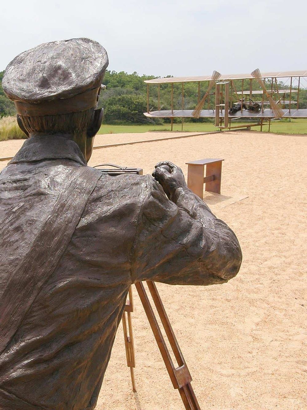 Bronze statue of a photographer taking pictures of a vintage airplane outdoor exhibit.