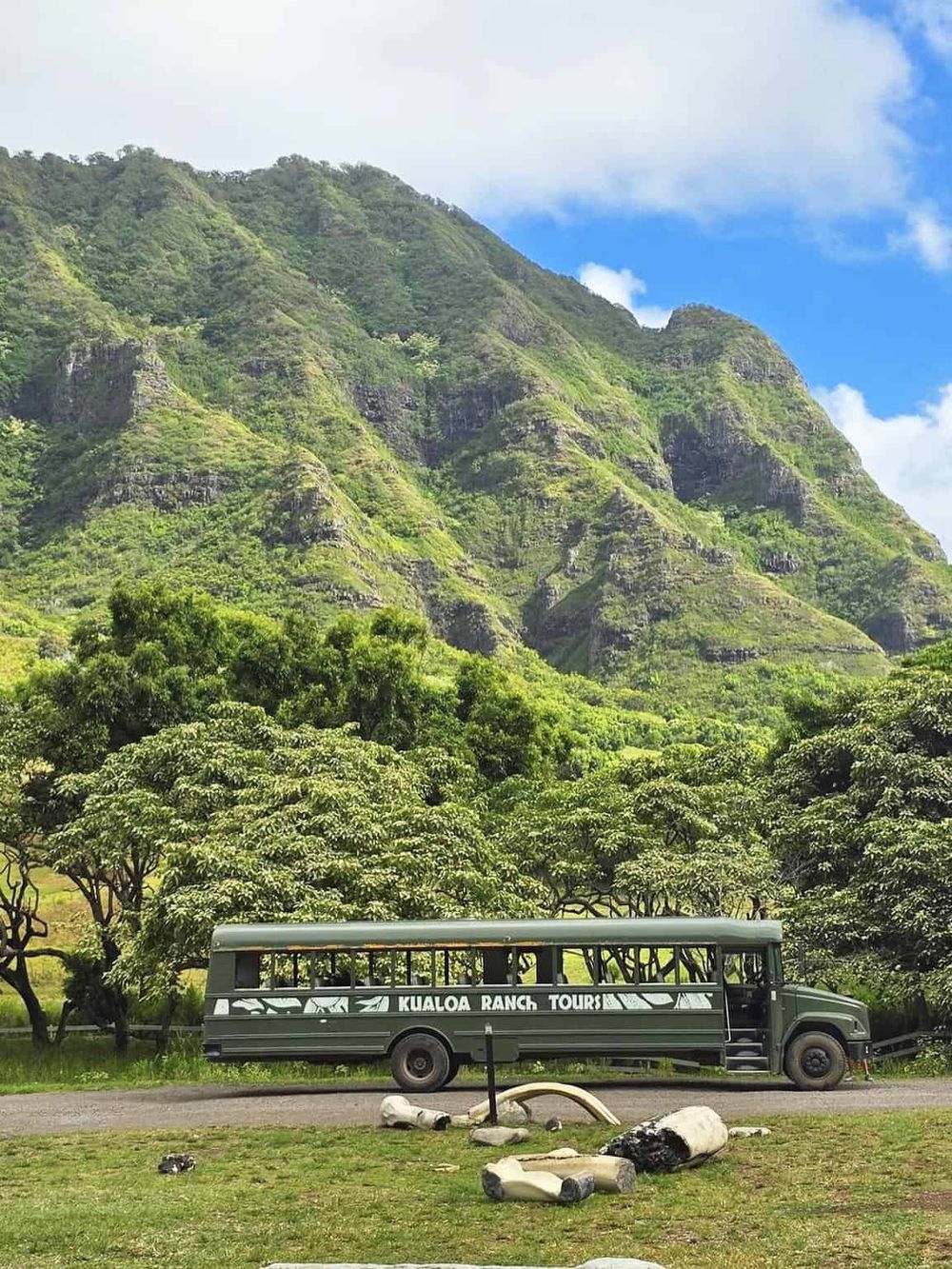 Lush green mountain scenery with a Kualoa Ranch tours bus in the foreground, Hawaii's outdoor adventure destination.
