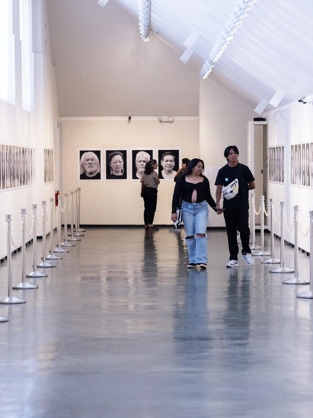 Empty art gallery with portraits, visitors exploring contemporary art pieces, and well-lit spacious interior.