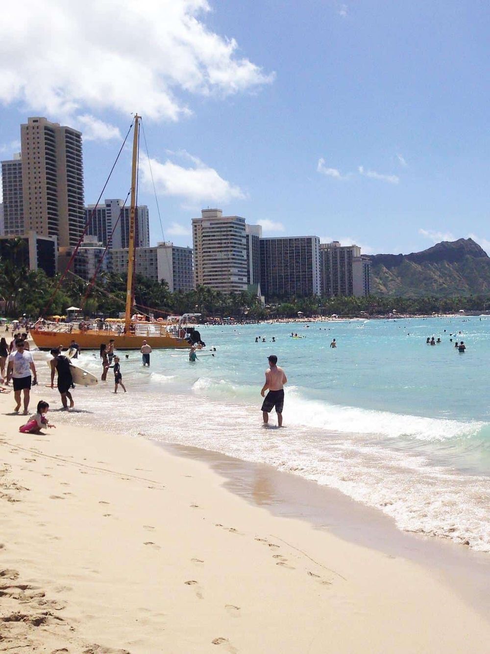 Bright urban beach scene in Honolulu with skyscrapers, clear blue water, and people enjoying the sun and surf.