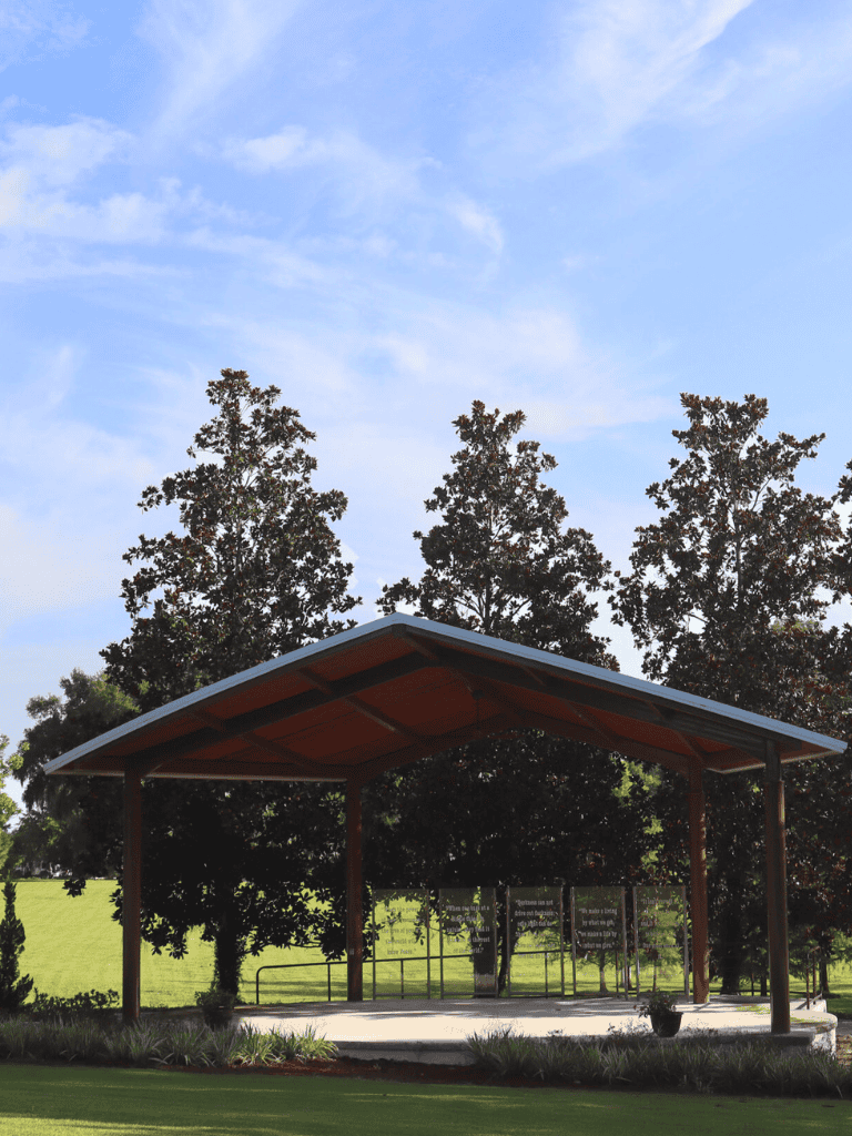 Modern outdoor shelter with roof, surrounded by trees, offering shade and relaxation.