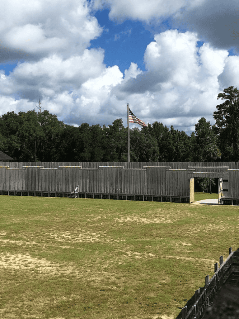 American flag on a pole in a park with cloudy sky and fenced area, outdoor community space.