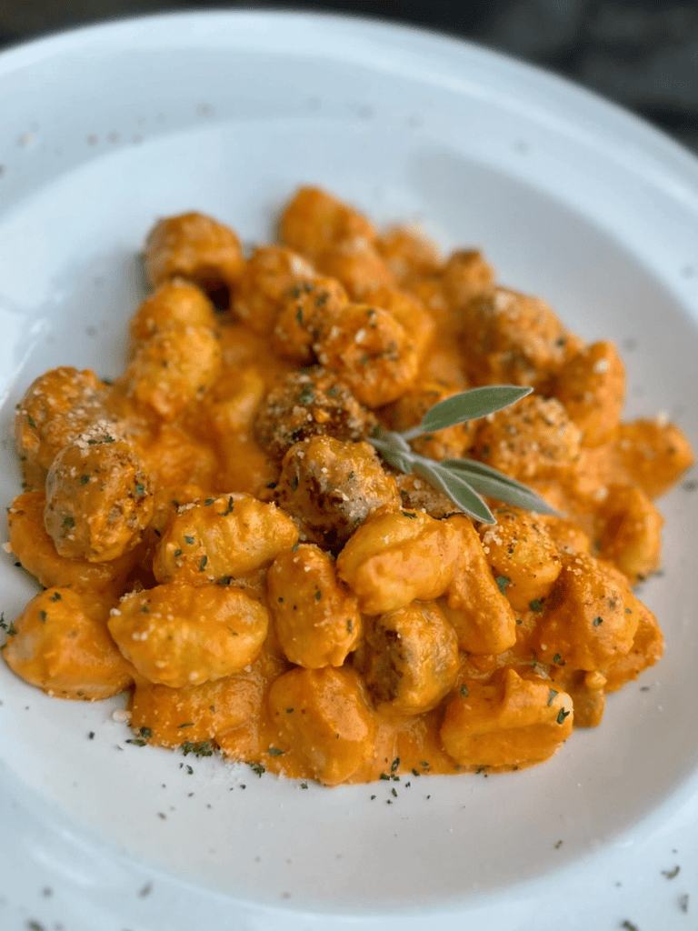 Creamy buffalo chicken gnocchi with herbs on white plate, flavorful comfort food.