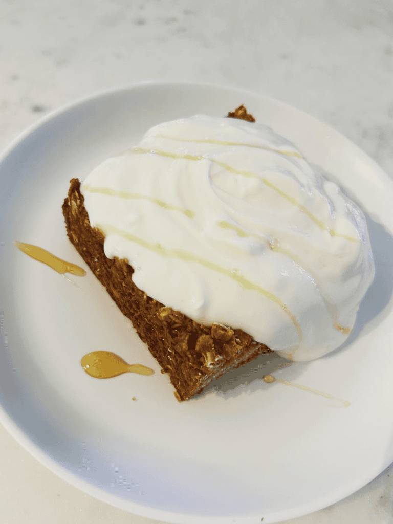 Creamy cheesecake topped with whipped cream and caramel drizzle on a white plate.