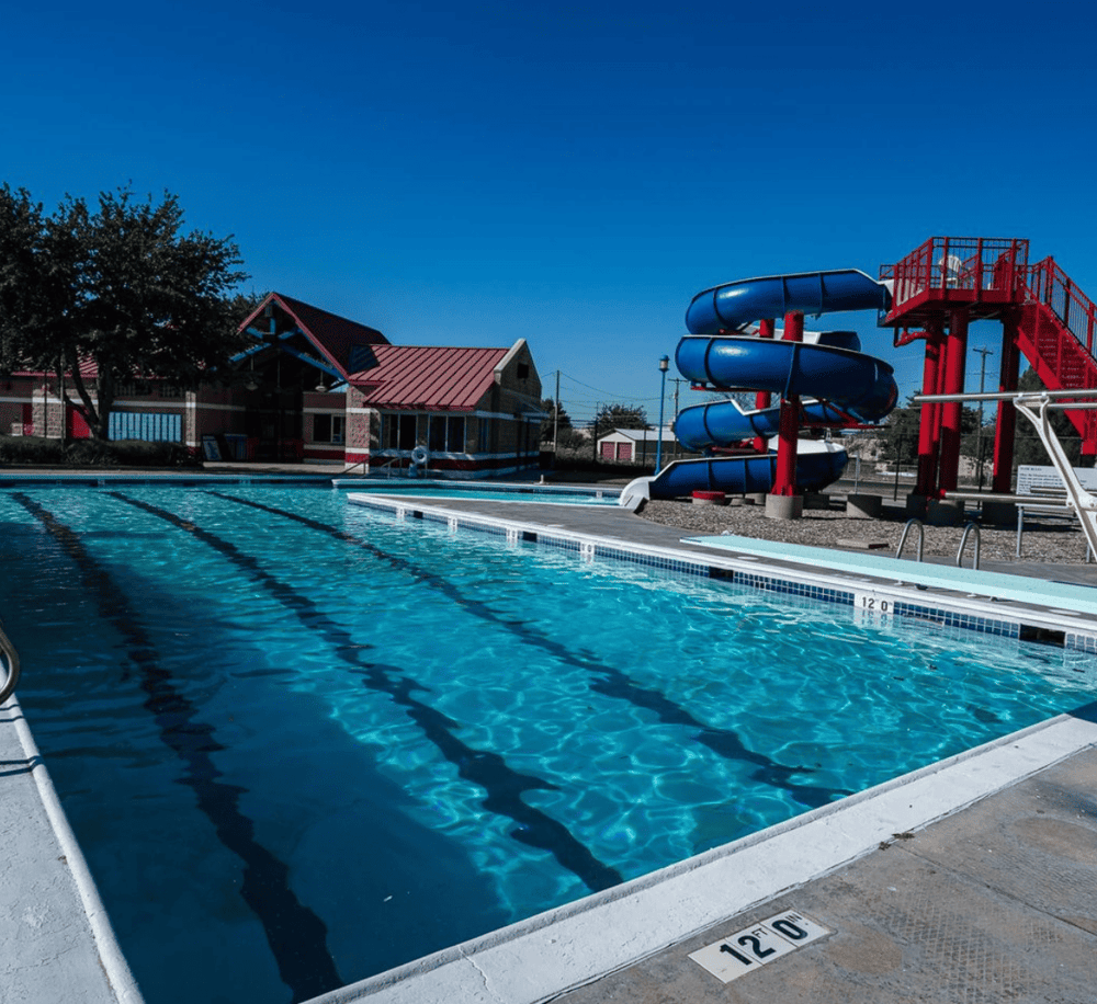 Bright outdoor community pool with water slide and splash pad, ideal for family fun and relaxation.
