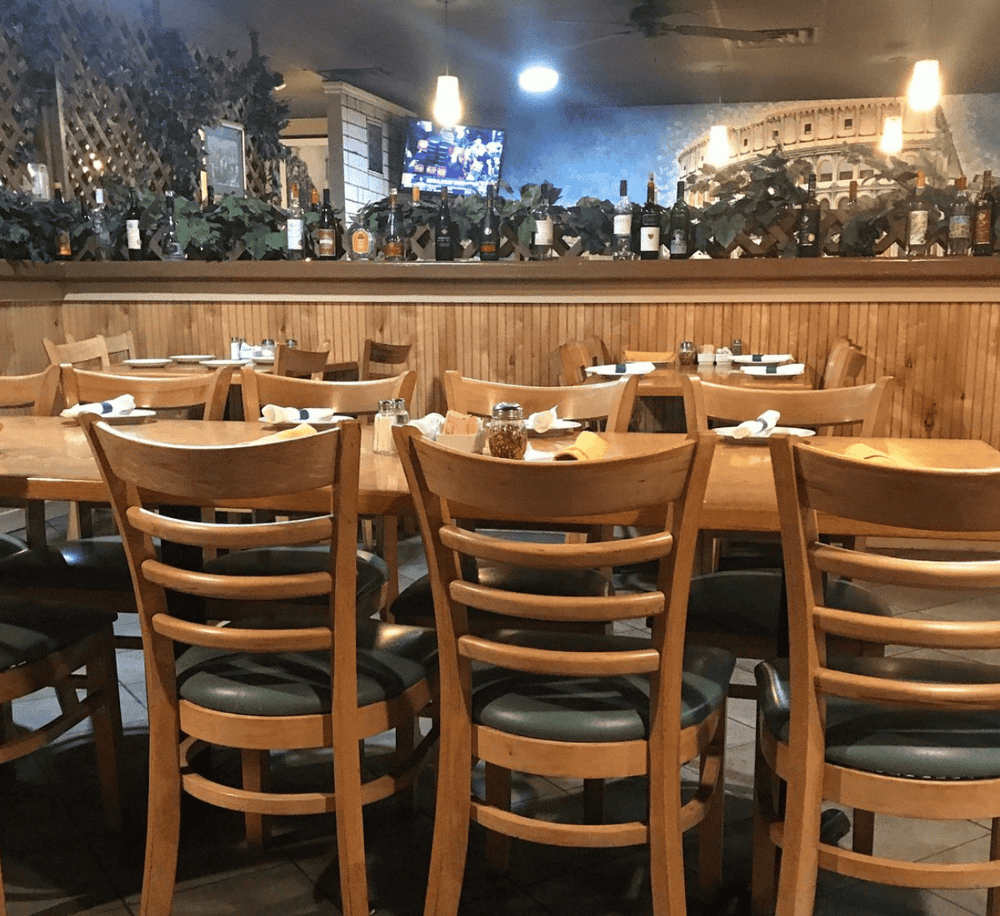 1. Cozy restaurant interior with wooden chairs and a bar area decorated with wine bottles and greenery.
