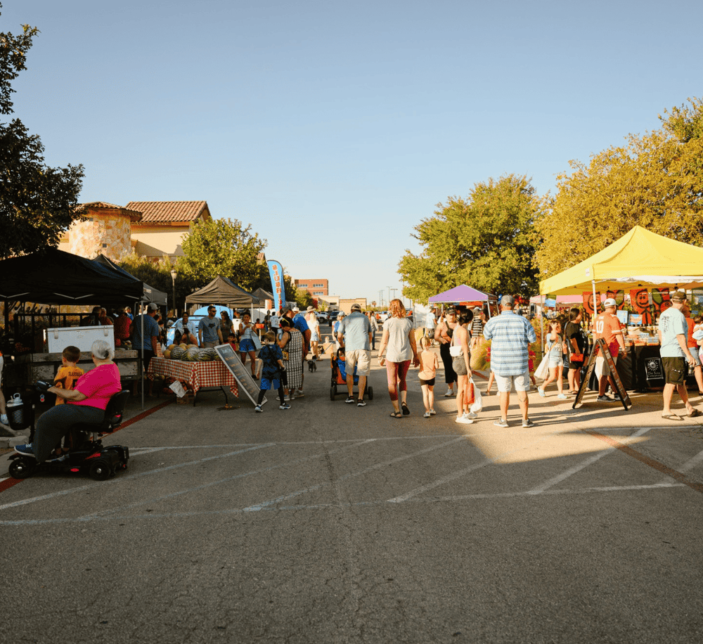 Outdoor community market with vendors and shoppers, vibrant atmosphere, and family-friendly activities.