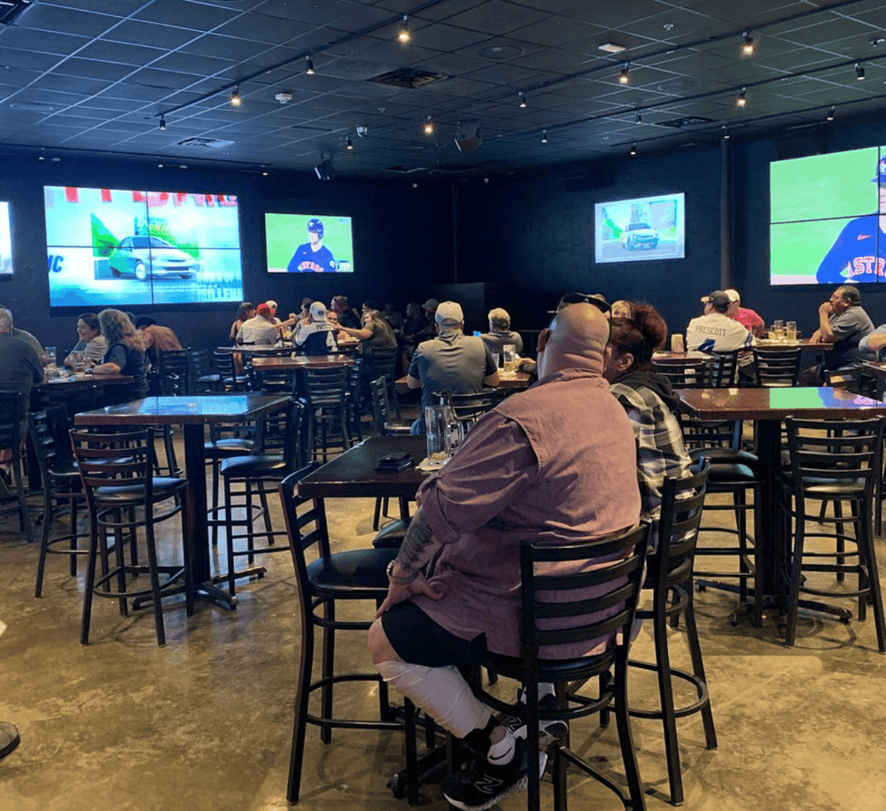 Watching sports at a sports bar with multiple screens, lively atmosphere, and diverse crowd.