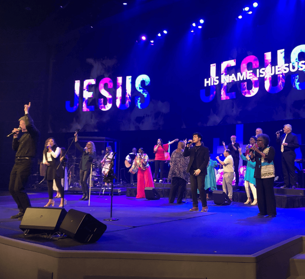 Vibrant church choir performing on stage with large "JESUS" sign in background, promoting Christian worship.