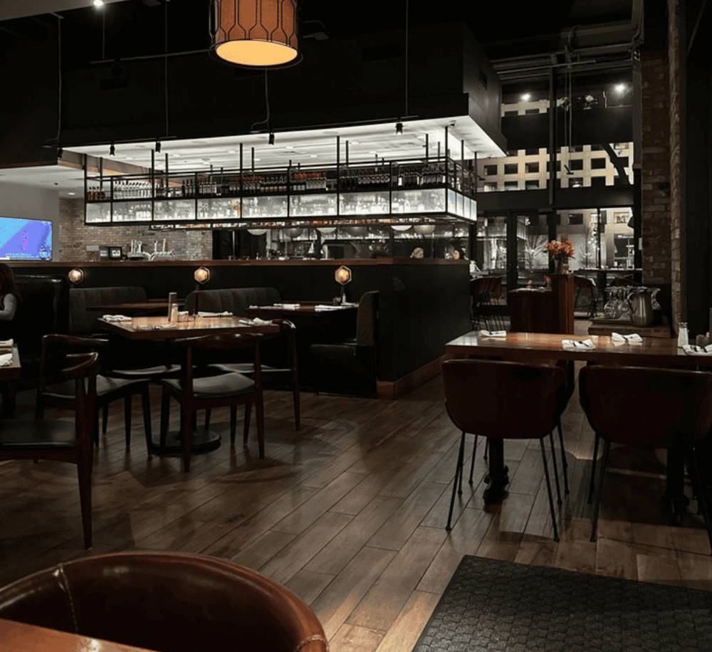 Cozy modern restaurant interior with wooden tables, stylish lighting, and a sleek bar area for dining and socializing.