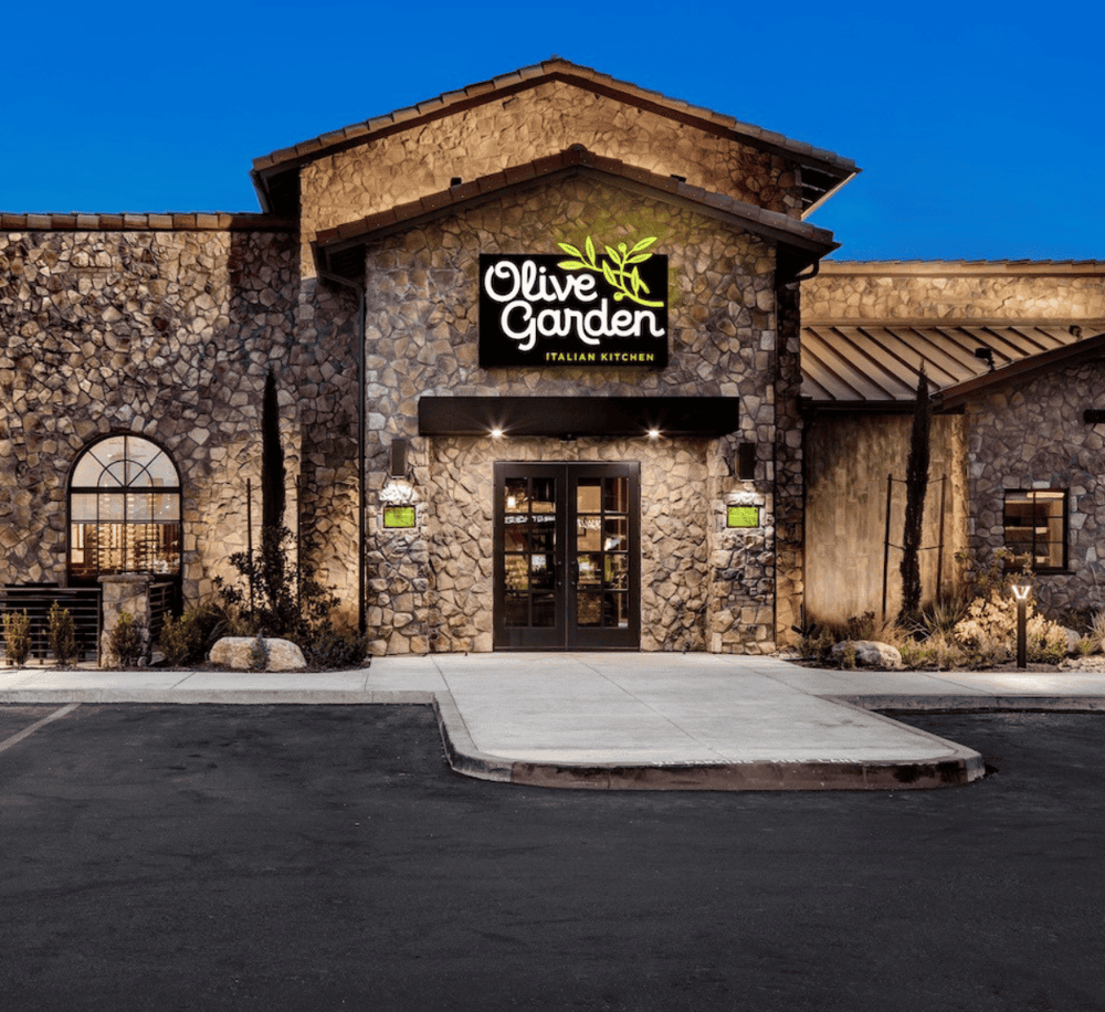 Elegant Italian restaurant Olive Garden exterior at dusk, showcasing rustic stone facade and inviting entrance.