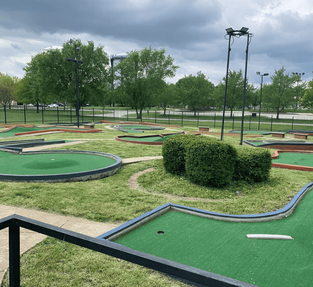 Miniature golf course with lush greenery and overcast sky at Quest for Directions. Enjoy outdoor mini golf fun in a scenic setting.