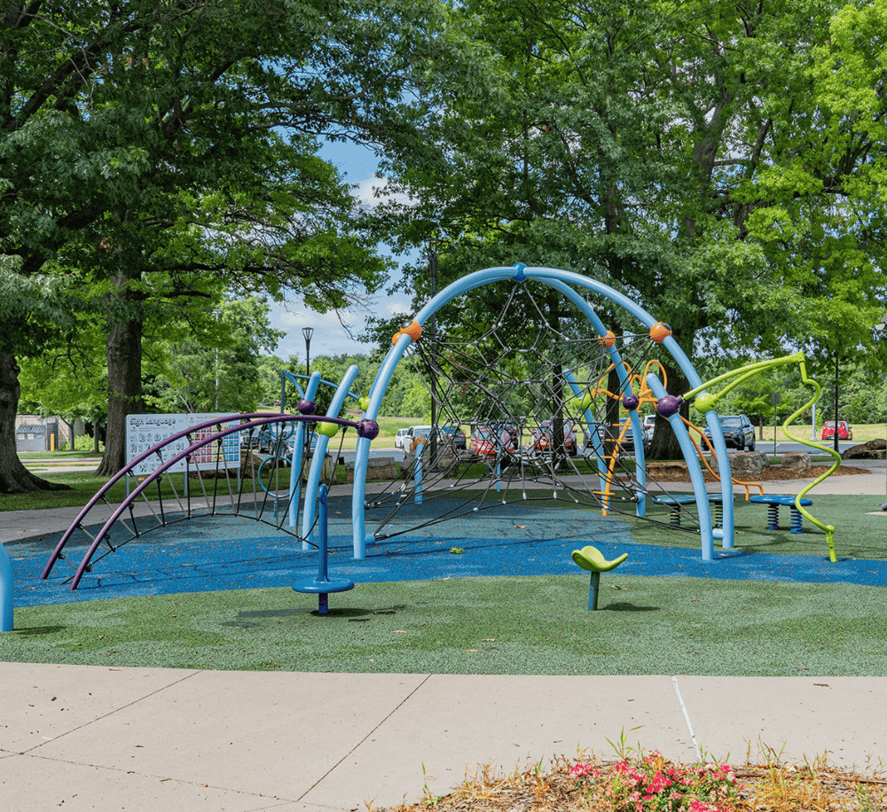 Colorful playground equipment in park with lush trees and safety surface, ideal for children's outdoor recreation.