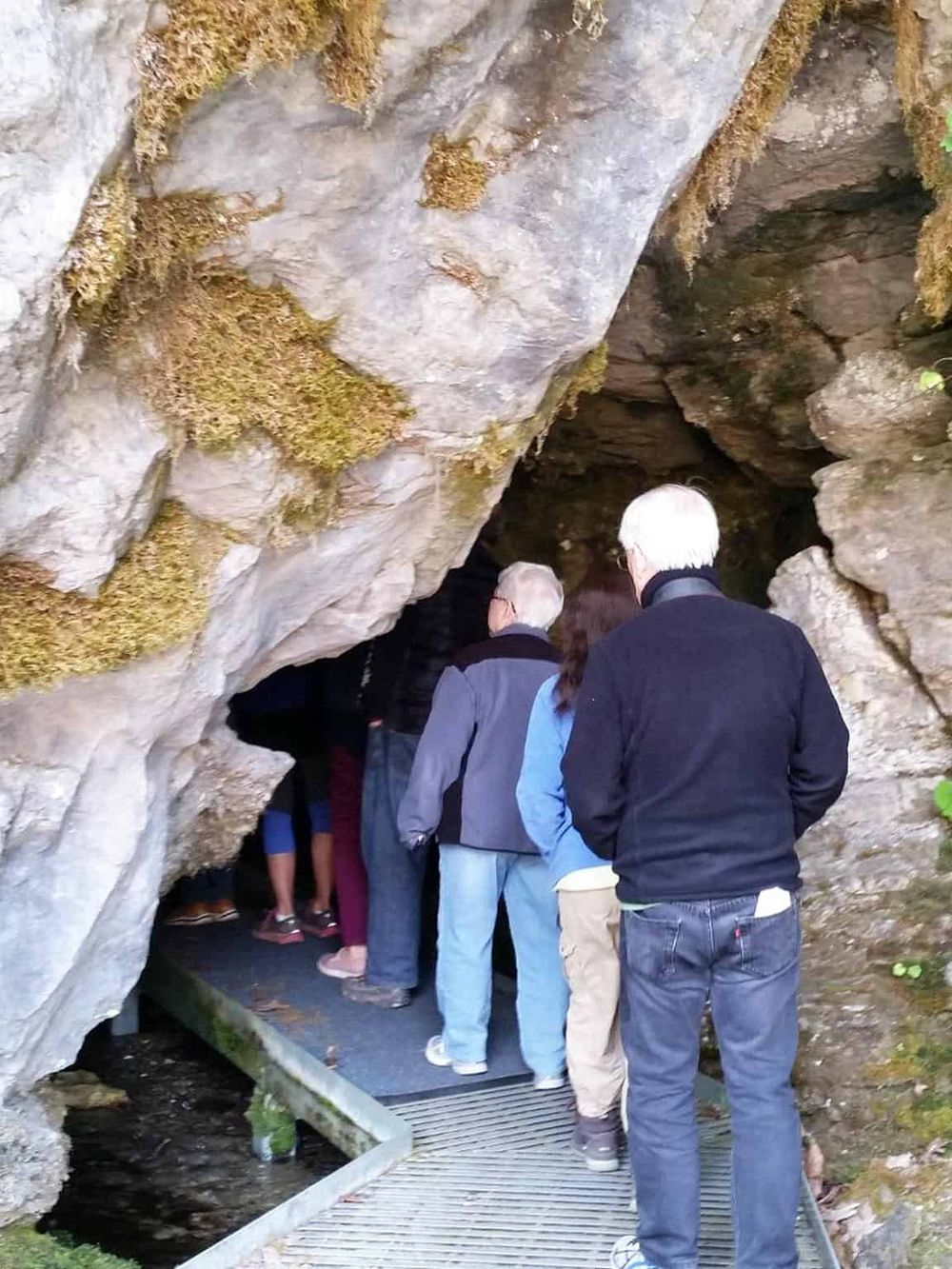 Underground cave exploration with a group of people walking through a rocky cave tunnel.