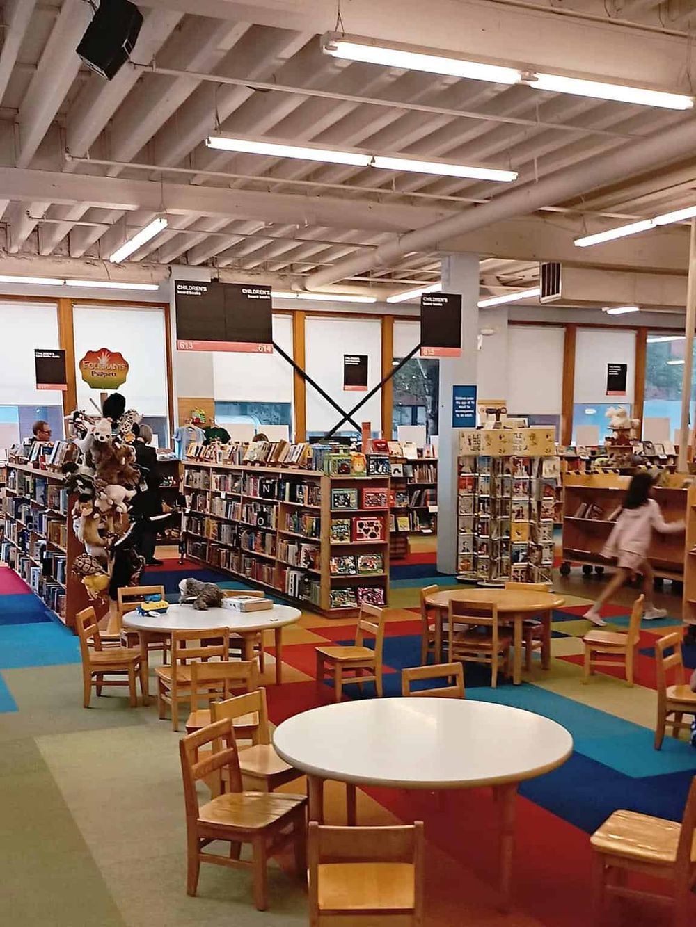 Brightly lit children's bookstore with colorful carpet, bookshelves, and cozy seating areas, ideal for storytime and kid-friendly shopping.