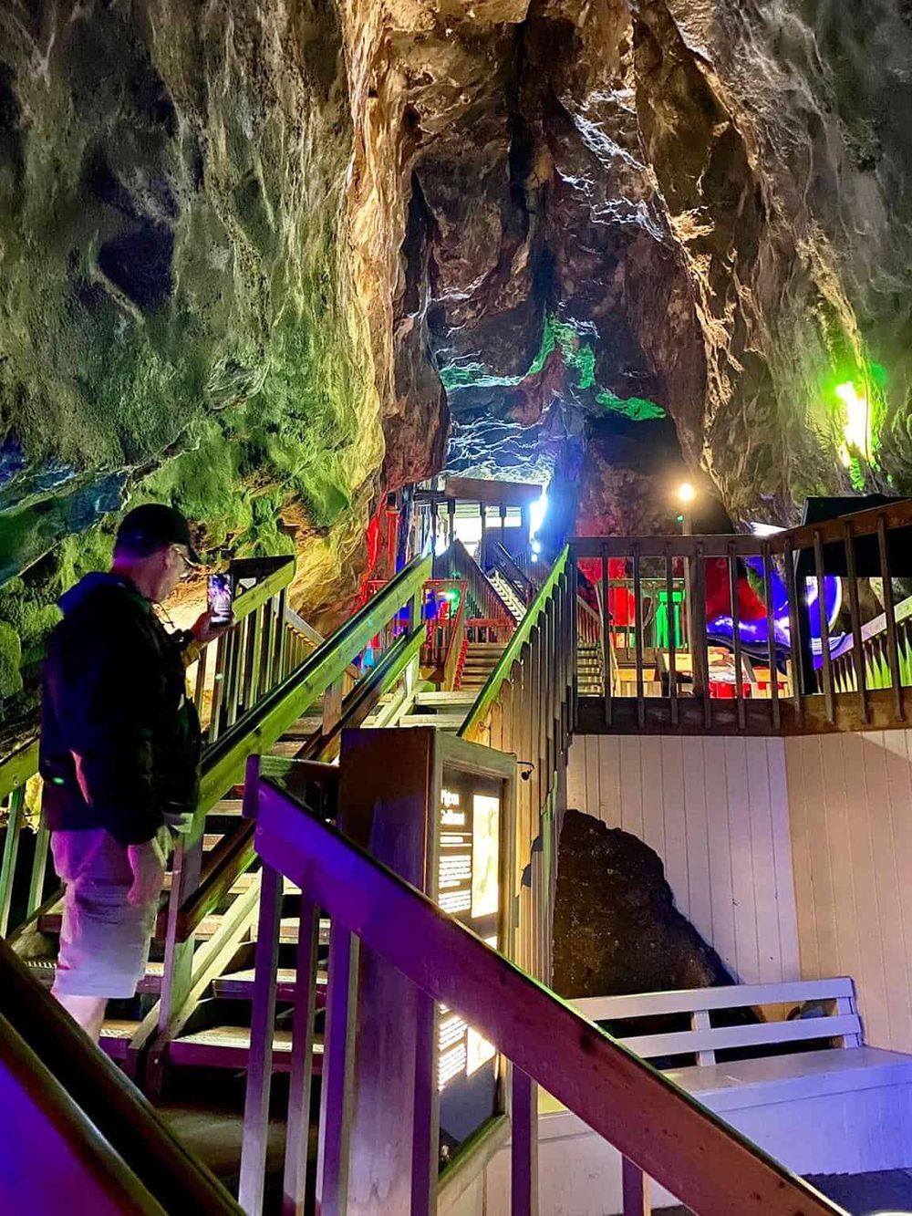 Vibrant underground cave with colorful lighting, wooden stairs, and visitors exploring the unique natural attraction.