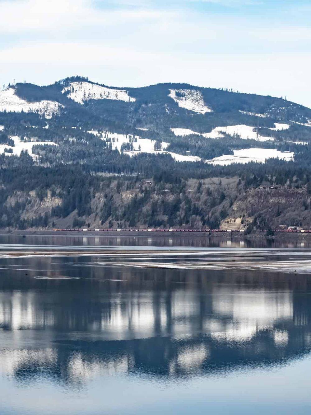 Snow-capped mountains reflecting on calm water during daytime.