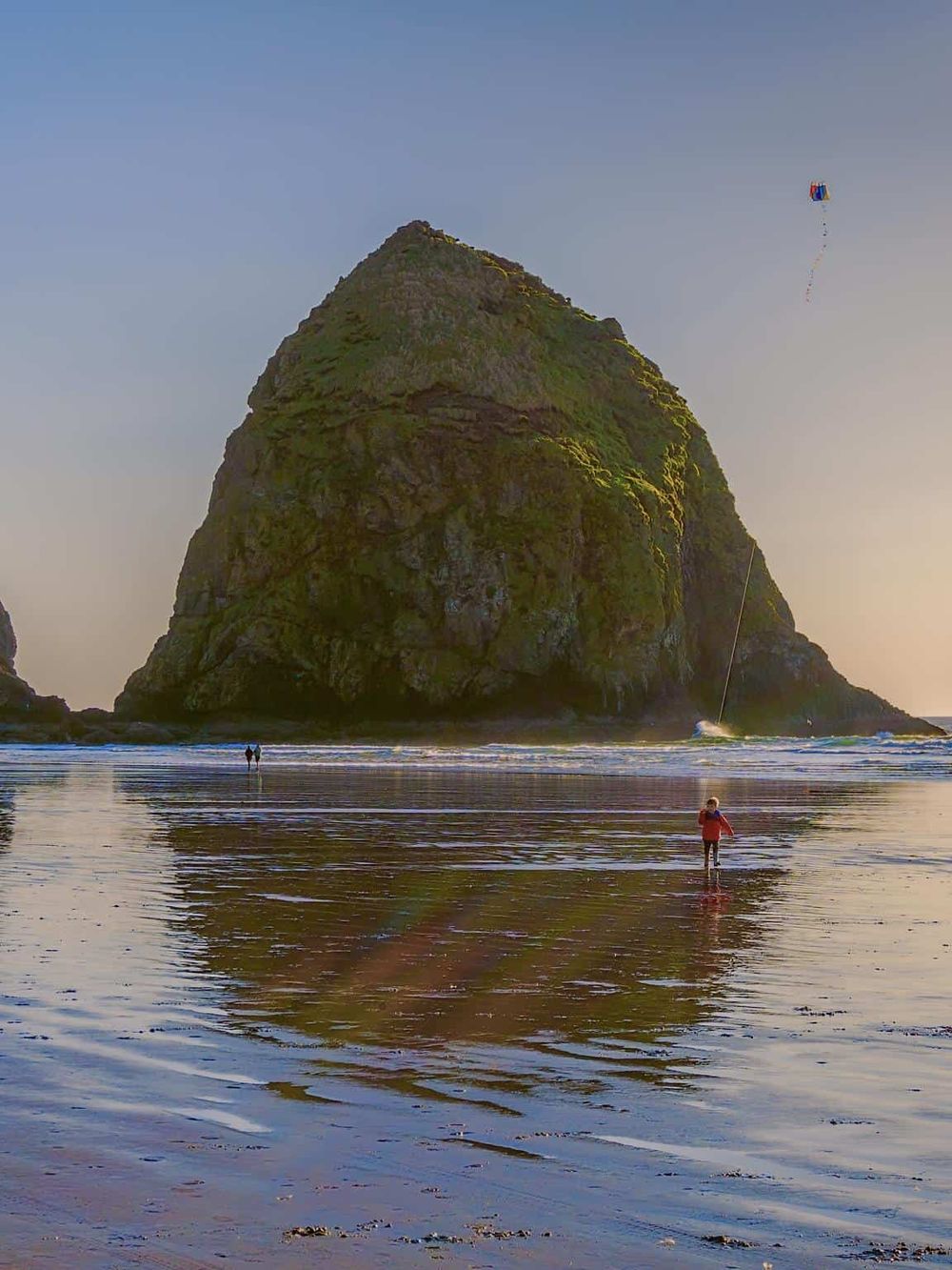Seaside rock formation with people flying kites at the beach, scenic coastal view, outdoor adventure, and travel destination.