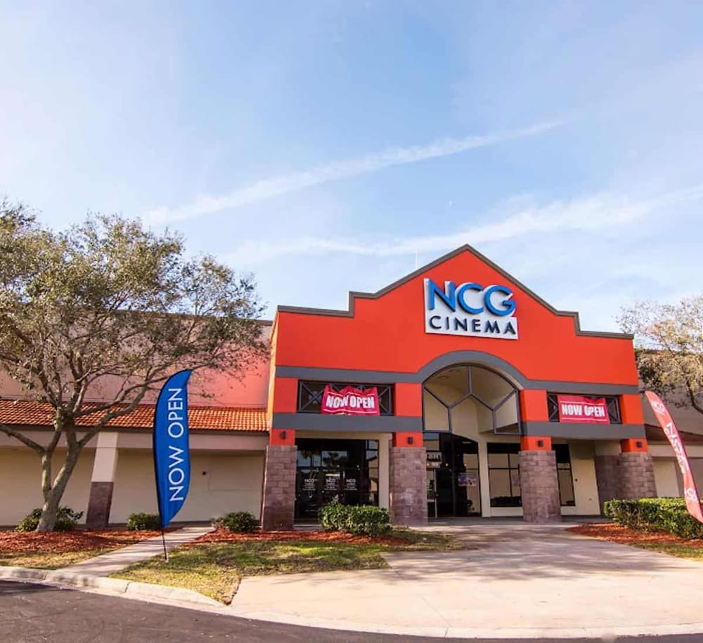 Bright orange NC CG Cinema building with "Now Open" banners, inviting moviegoers to enjoy the latest films.