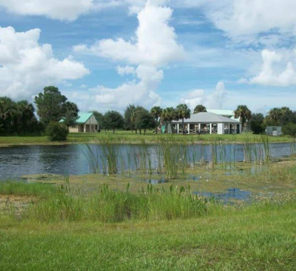 Serene lakeside scene with modern house, lush greenery, and blue sky, perfect for outdoor relaxation and scenic views.