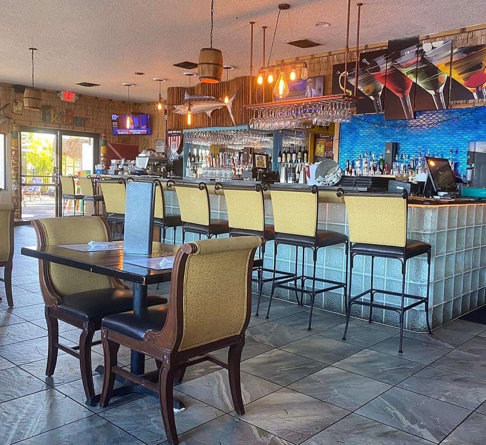 Bright bar and dining area featuring a tropical decor, modern lighting, and a variety of seating options at a restaurant.