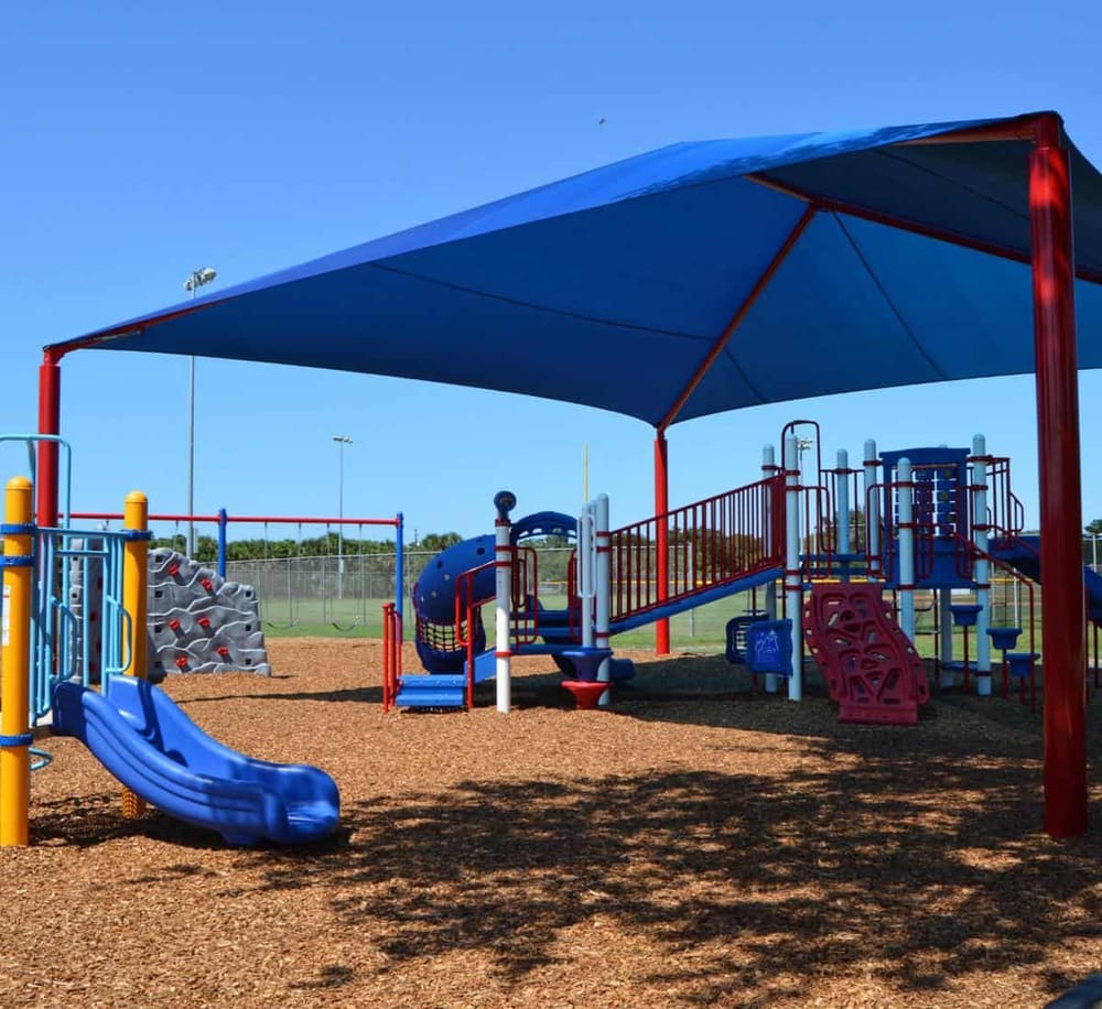Colorful outdoor playground with slides, climbing structures, and shade for kids' recreation.
