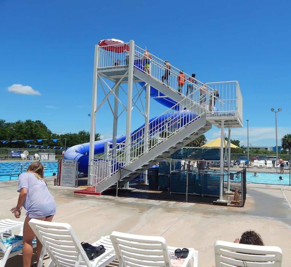 Water slide at outdoor pool with kids enjoying sunny summer day.