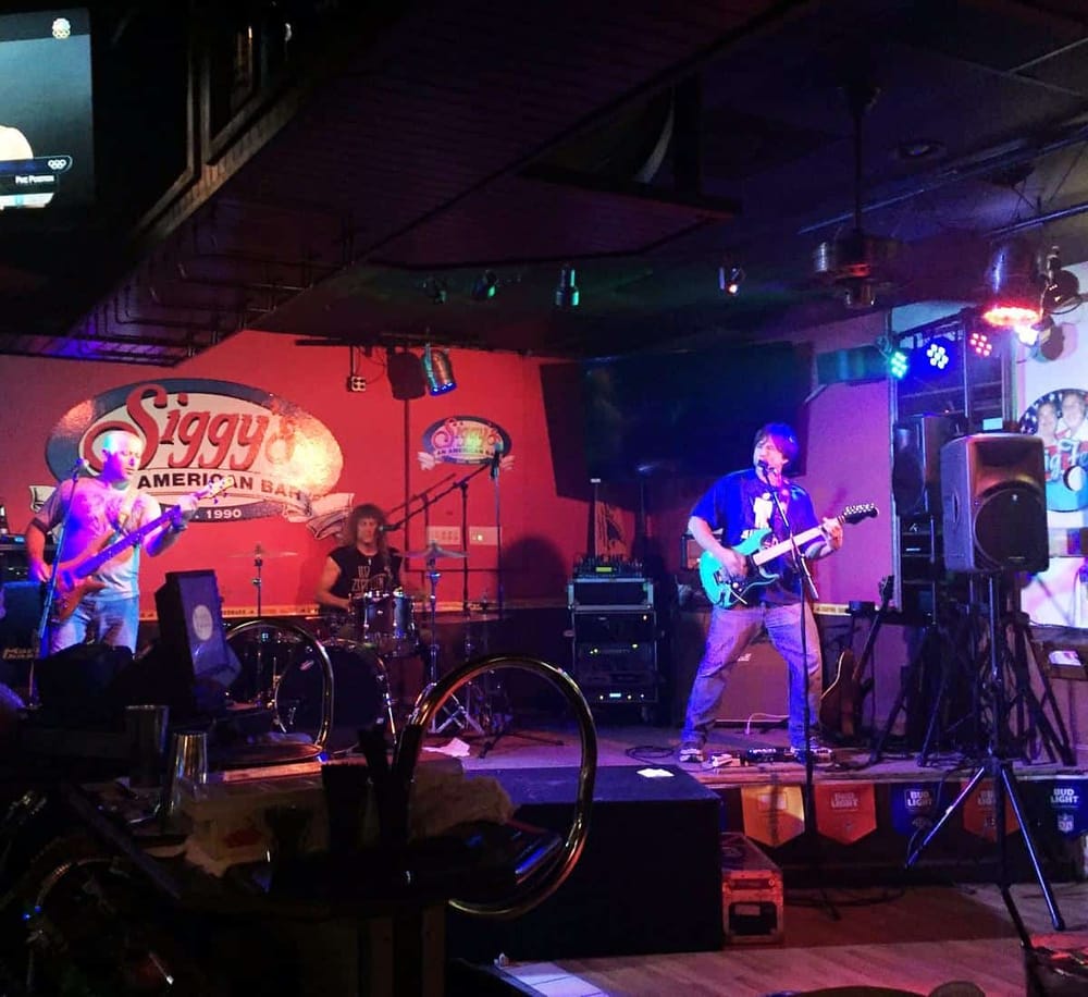 Vibrant live music performance at Siggy's American Bar, showcasing band members playing guitars and drums.