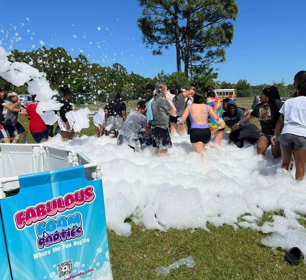 Children having fun at a foam party outdoor event with foam machines and a colorful signboard.