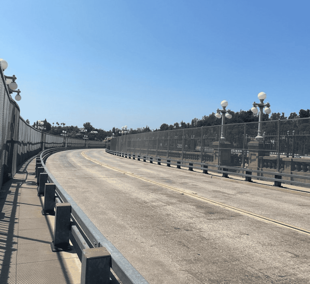 Open-air pedestrian bridge with decorative lamp posts and safety fencing, scenic view.