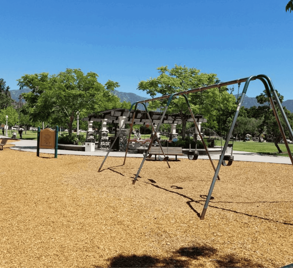 Swings in a neighborhood park with trees and mountain views in the background.