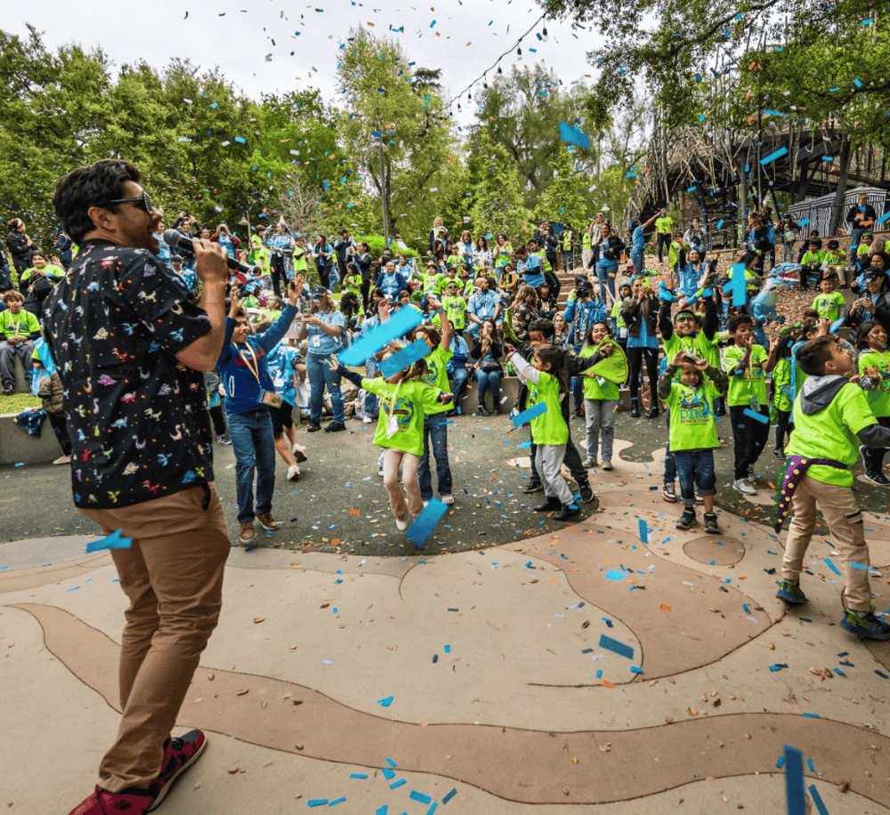 Kids celebration event at QuestForDirections outdoor venue, lively atmosphere, confetti, children in bright green shirts.