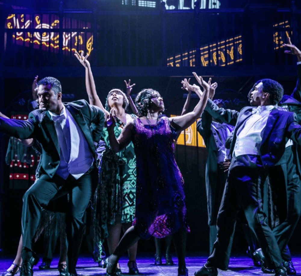 Vibrant musical theater performance with dancers and singers on stage, showcasing dynamic choreography and colorful costumes.