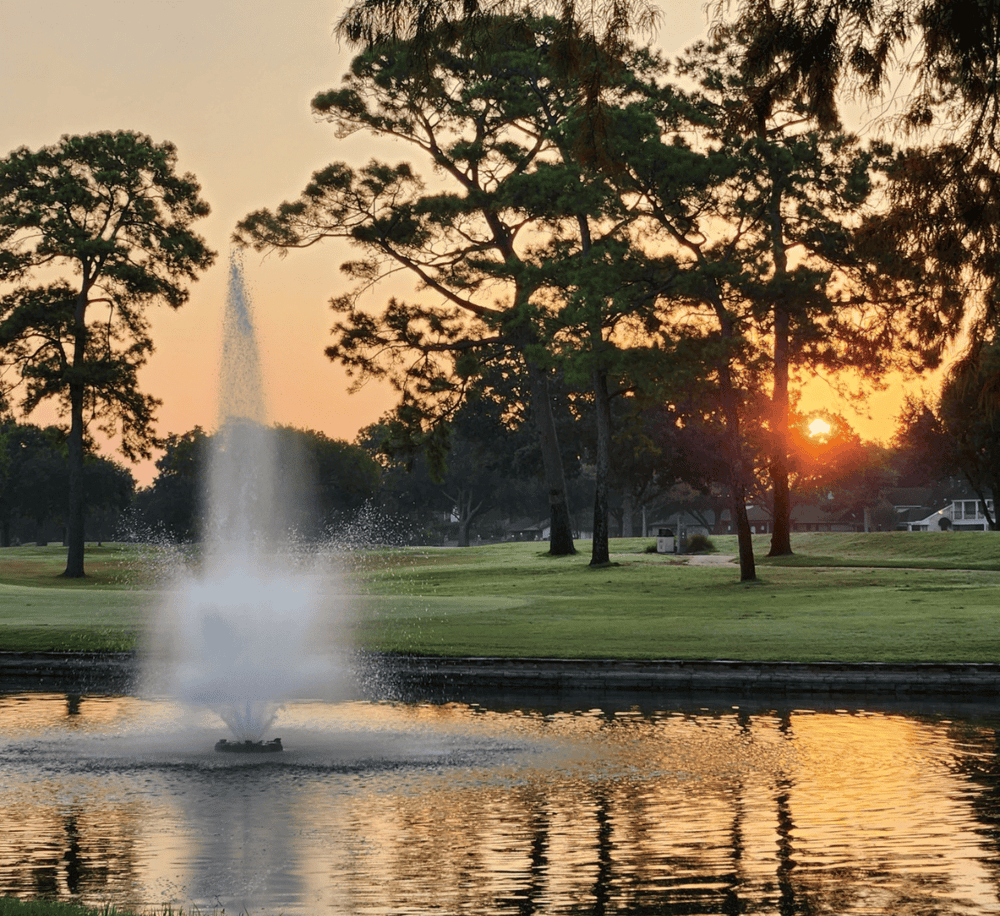 Serene golf course at sunset with fountain and water reflection, peaceful outdoor scenery.