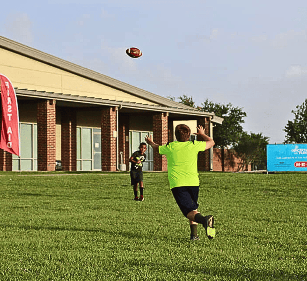 Youth football players catch football during practice on a grassy field.