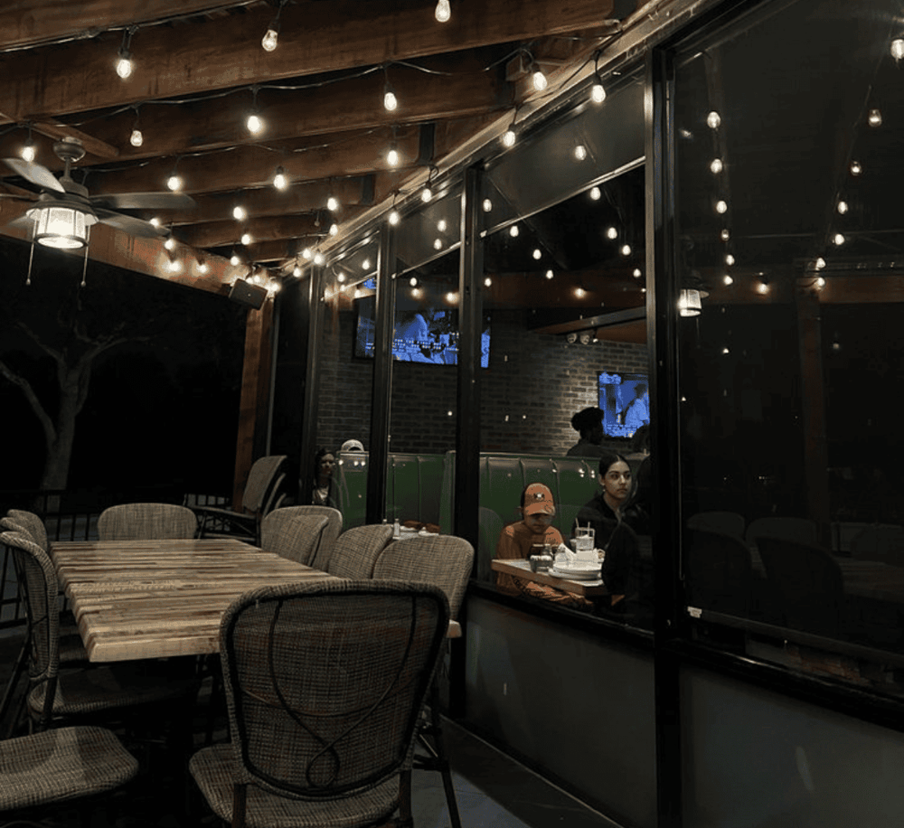 Cozy restaurant with string lights, wooden ceiling, and large glass windows at night.