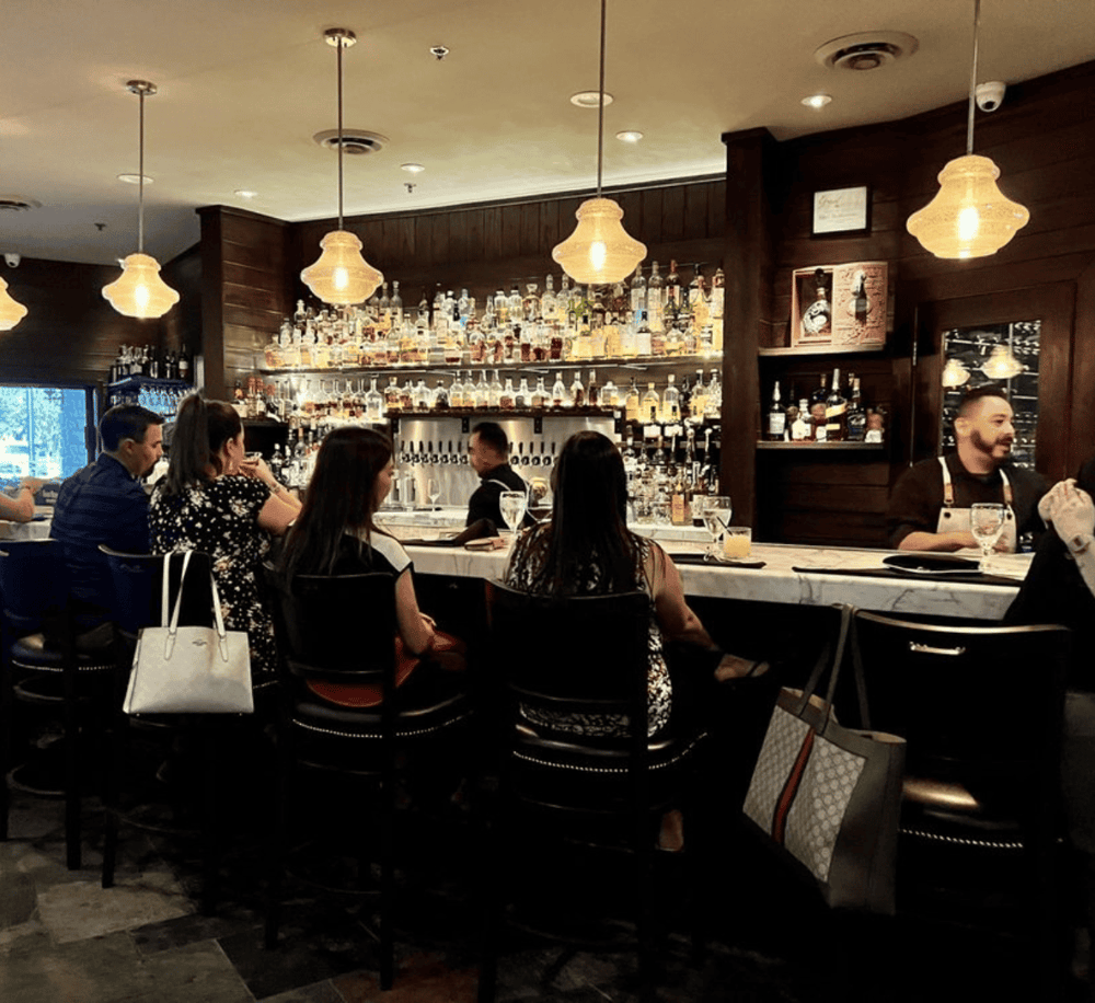 Elegant bar interior with guests enjoying drinks and bartender serving patrons.