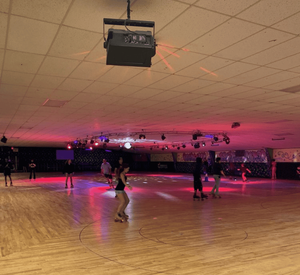 Brightly lit indoor roller skating rink with colorful lighting and people skating.